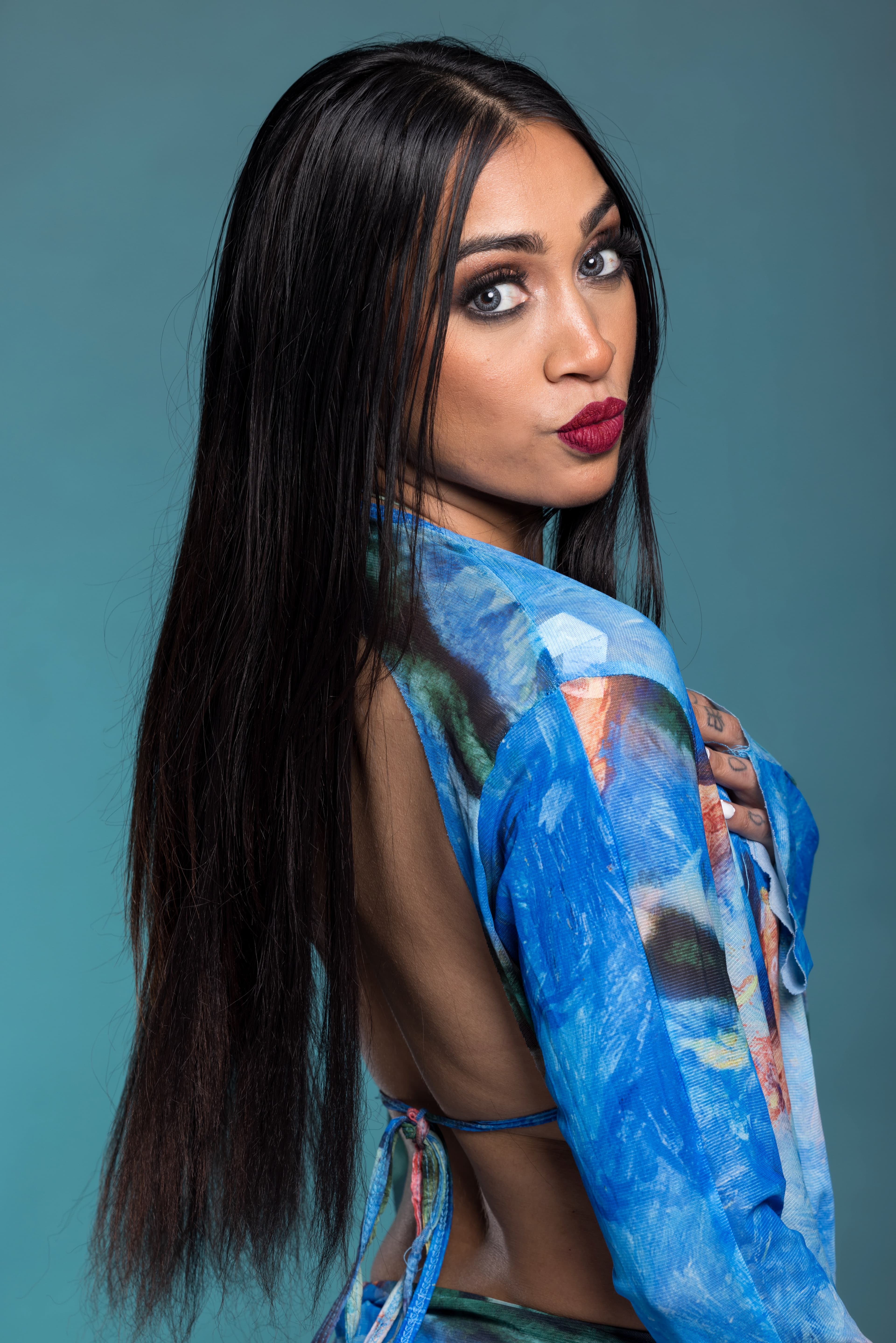 Over-the-shoulder studio portrait with a smoked bronze eye and deep berry lip
